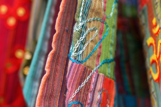 close up photograph of colourful bags for sale.  One of them is a green, pink and purple striped fabric with embroidery on it. 
