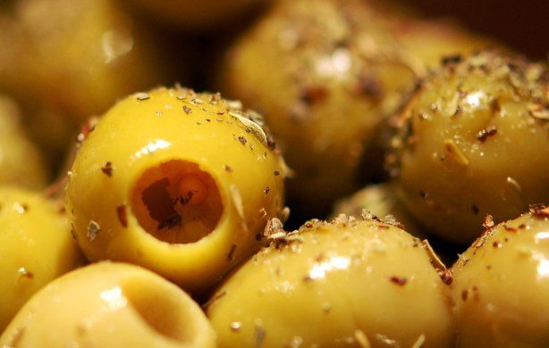 many green pitted olives that are covered with oil and dried herbs and spices