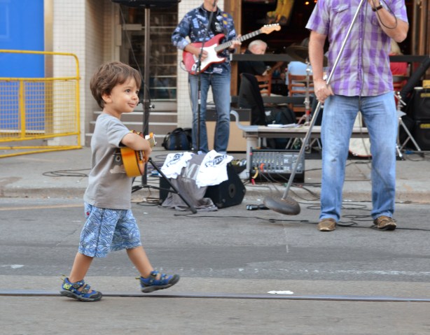 boy with toy guitar walking in front of a live band