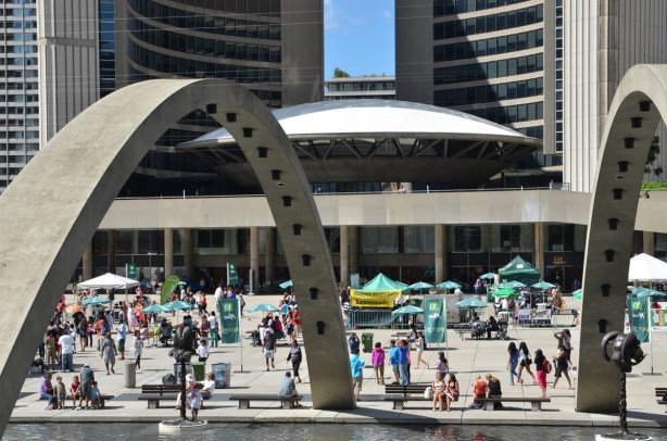 Nathan Phillips Square from the south, showing one of the arches over the fountain. Some vendors are there as well as some tourists and other people enjoying the sunny afternoon. 