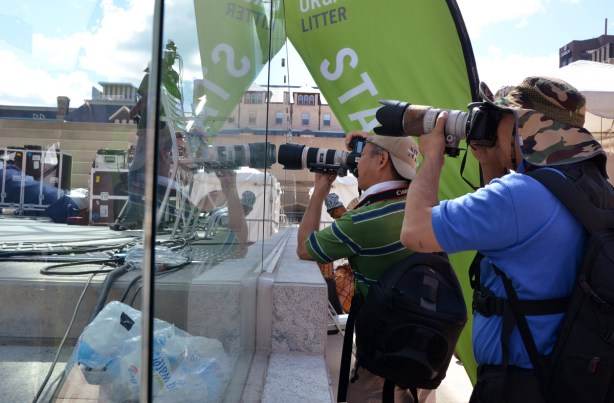 Two Asian male photographers and their cameras with very long lenses taking pictures of a performance on the stage at Nathan Phillips Square.  