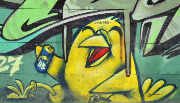 Uber's yellow bird is laughing and drinking something from a can.  Somone has added the words grain fed to his forehead.