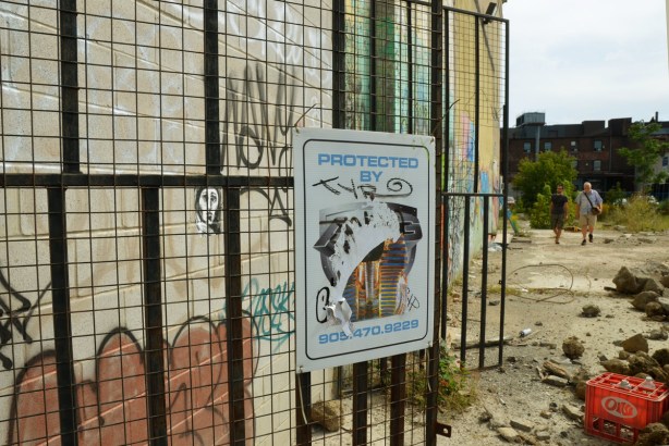 two wire gates. One has a sign on it that says 'protected by' but the name of the company is obscured by a tag