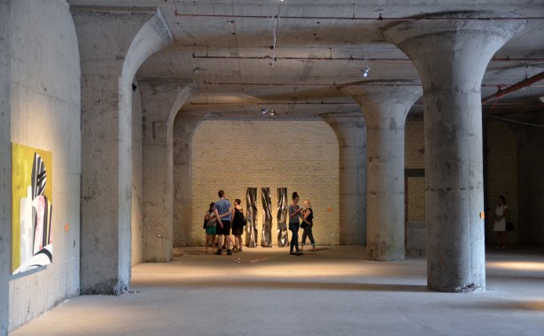 a group of people looking at a piece of art. They are in a large open space that once was a factory. Concrete and brick walls.
