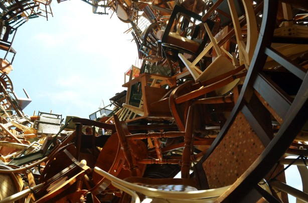 A hollow pile of chairs about thirty feet high.  The photo is taken from inside the pile.  The sky can be seen in the photo. 