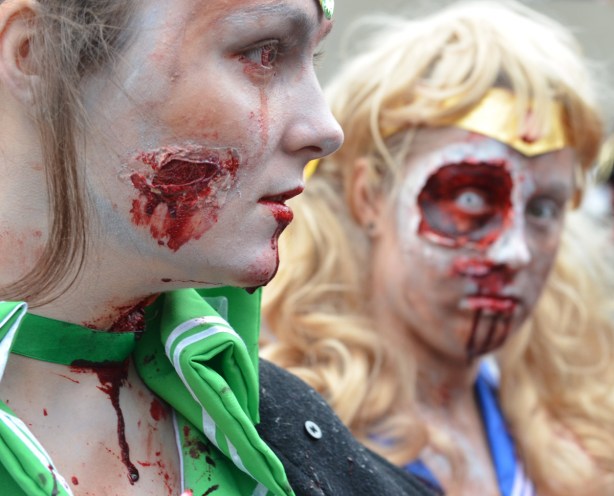 two woman dressed up like zombies.  The woman in the foreground has blood dripping off her chin and down her neck.  The woman in the background has a large ugly facial wound