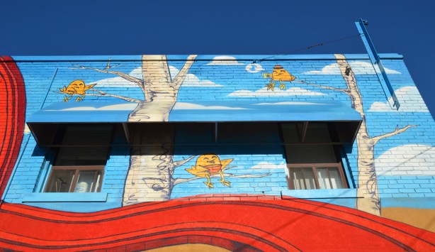 part of the mural by uber 5000 showing three uber chickens sitting on tree branches. This part of the mural is on the second storey and it includes the awning over a couple of windows. 