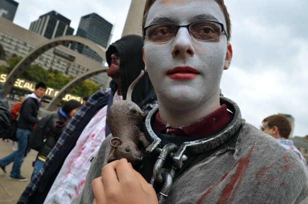 A man with white makeup on his face, a chain around his neck and a plastic rat on his shoulder.