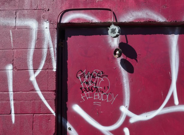 A wall and door have been painted a maroon colour.  Someone has written the words Hi Buddy on the door.  There is a light fixture over the door but it is broken.