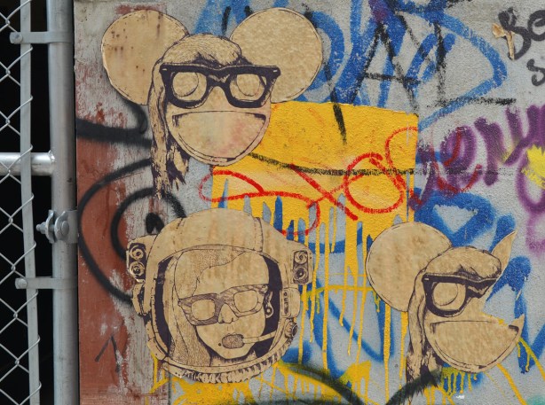 a brown and black set of posters/stencils of three heads.  Two are the same - they look like heads with big ears and they are wearing very big sunglasses.  The third looks like a woman in a helmet like the kind an astronaut might wear.