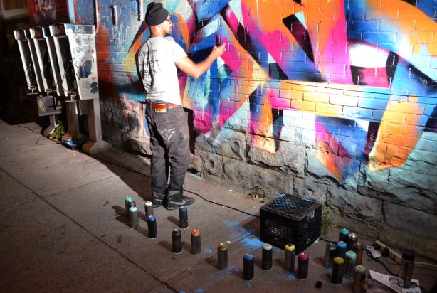 A man is spray painting a piece of street art using aerosol cans of paint