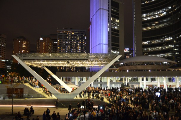 crowds and lights at Nathan Phillips Square. Toronto city hall is lit with purple lights.