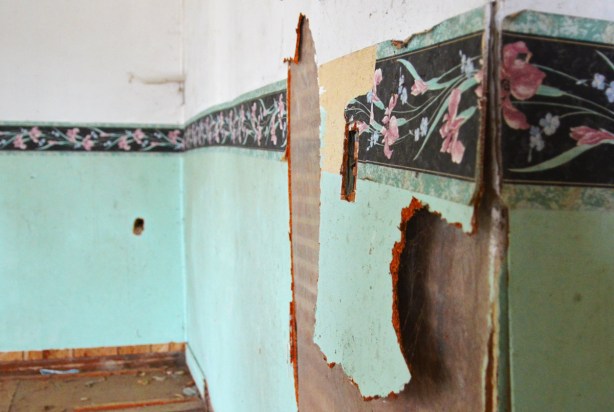 The light teal coloured wallpaper is falling apart on an interior  wall.