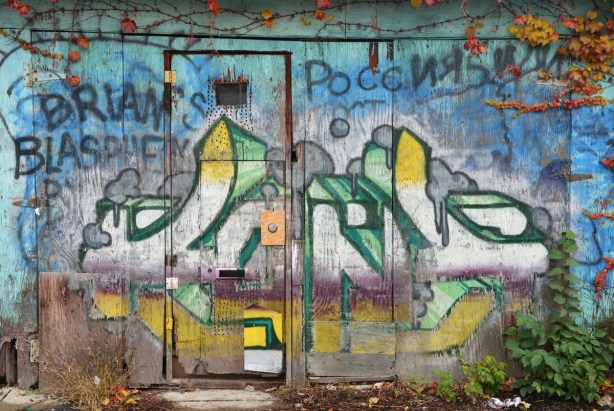 An old wood door and wall with faded graffiti on it. 