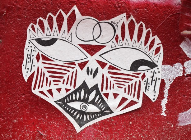 A stencil graffiti of a stylized face in black and white.  It is on a very red wall. 