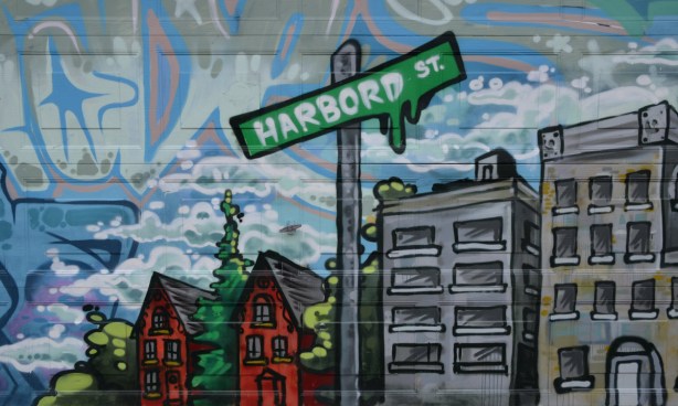 mural showing two red brick houses, a small grey apartment building and a green street sign that says Harbord St.