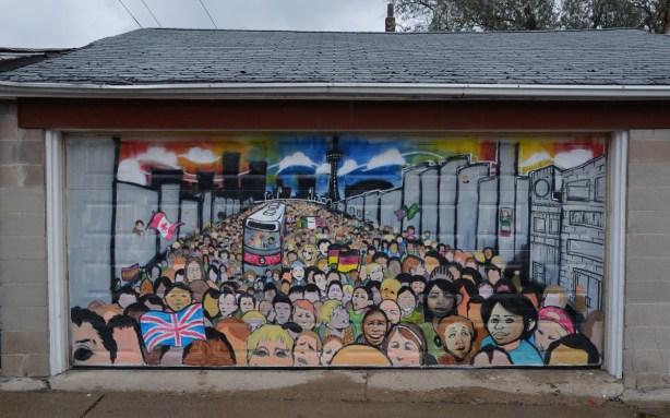 Mural on a garage door showing a large group of people of many different races.  There is a TTC street car in the center of the crowd.  Some people are waving flags - a Canadian flag, a German flag, and a Union Jack 
