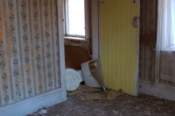 An old toilet lies on its side in the doorway of an abandoned farm house. 