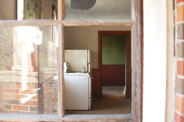 Two small window panes in a door are broken, there is no glass.  When you look through the window you see into the kitchen where there is a stove and a fridge. Otherwise, the house is abandoned. 