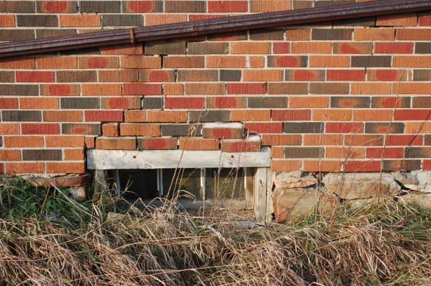 view of a basement window.  The wall is brick and the foundation is stone.  Some of the bricks near the bottom are starting to come loose. 