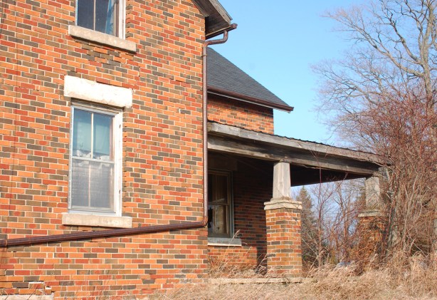 side view of a brick farm house showing the porch and a couple of windows.