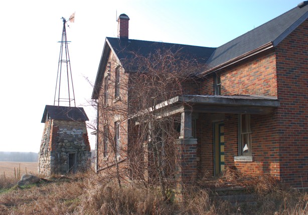 old abandoned farmhouse with windmill just behind it. 