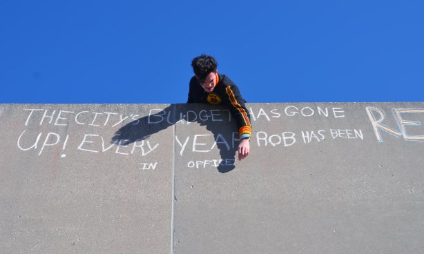 A man is writing with chalk on a grey concrete wall.