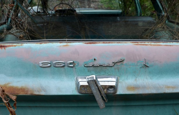 The back end of a rusty, once light blue, 660 Cross Country model of car