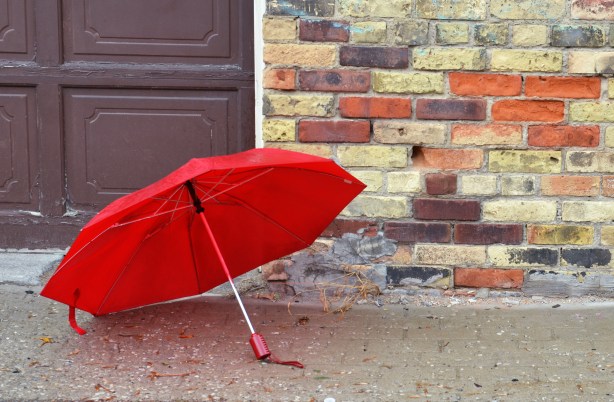 A red umbrella in front of a wall made of different coloured bricks - yellowish, orange, brown, and purple