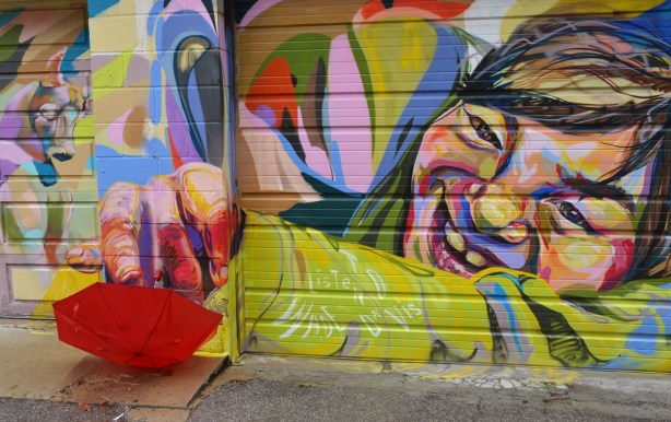 A mural on a garage door shows a girl reaching out her hand. The umbrella is placed by her hand.