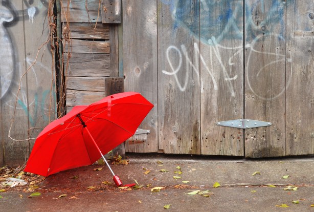A red umbrella on the ground beside a gate made of weathered wood