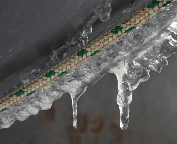 small icicles hanging from the side of a boat.  A braided beige and green rope runs along the side of the boat where boat meets ice.