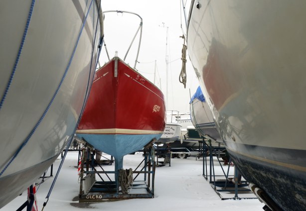 National yacht club, sailboats in their cradles, snow on the ground.  In the center of the picture is a blue and red boat with the name Gecko written on the side.  There are a number of other boats, most of which are white. 