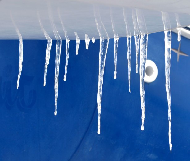 icicles hanging off the side of a blue and white boat.  Close up shot.