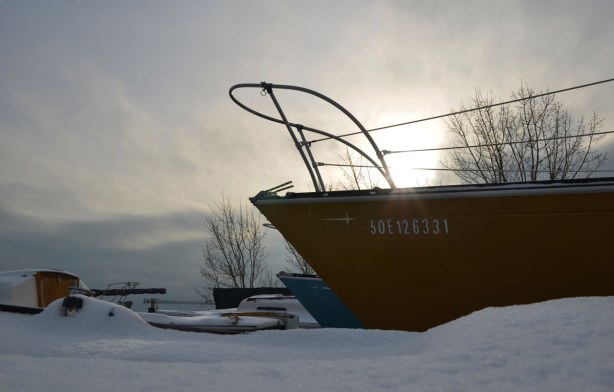 In the background the sun tries to shine through the clouds.  There is enough light that rays of sunshine bounce off the yellow hull of a boat that is in the foreground.
