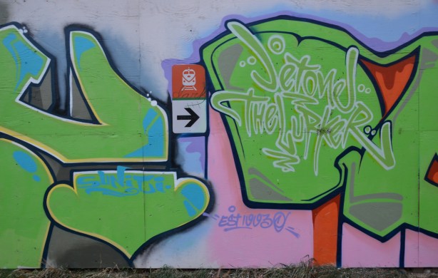 part of two green tags. A sign pointing to the train station entrance is in the middle. Someone has written the word dark on the sign. 
