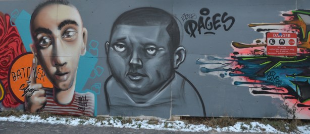 graffiti picture of the head and shoulders of two men. The one of the right is in shades of grey while the one on the left is a more natural colour. 