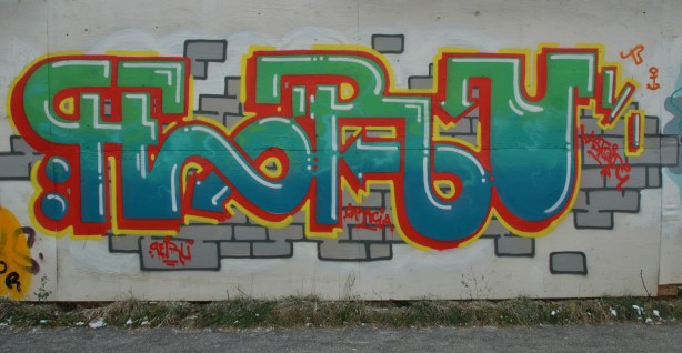 graffiti tag - stylized letters forming the word Peru in green, blue and red. Some grey bricks have been painted behind the letters. 