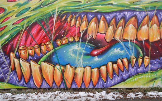 large graffiti picture of a close up of a mouth interior showing many orange teet, a blue tongue and purple gums. 
