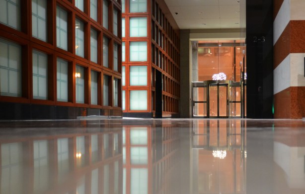 A wall and its reflection in the very polished and shiney floor.  The wall looks like a grid of brown wood surrounding pale blue glass squares. 