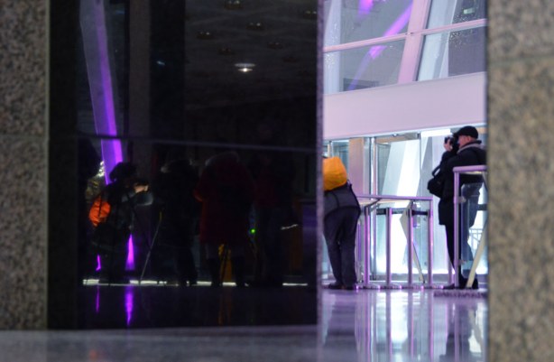 A group of photographers.  Some of them are reflected in the shiney black surface of the wall. 