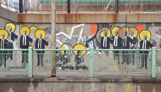 part of the suitman mural - many men in suits standing in a line. Three sitting women are in the middle. 