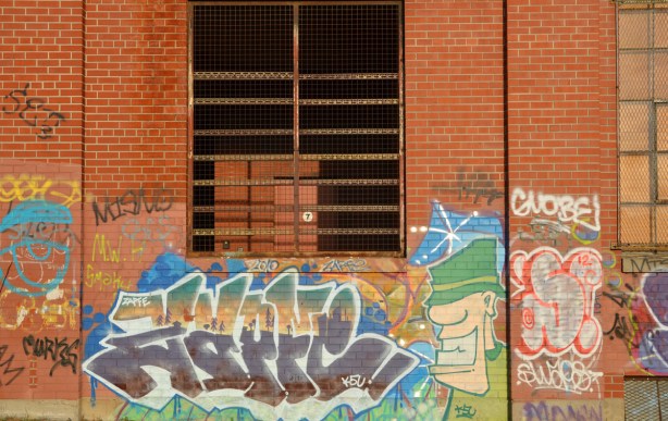 An open window covered with metal bars and a metal screen. Graffiti on the walls too.