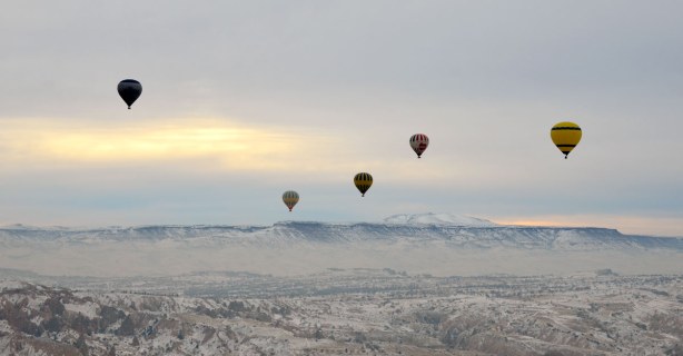 Five or six hot air balloons in the distance, all flying over a valley with mountains in the background.