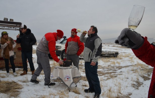 people standing around in a group drinking champagne. Outside, on a snowy field.