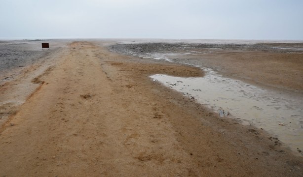 A view across the lake. It is flat as far as you can see. There is a road that appears to run out into the very shallow lake.