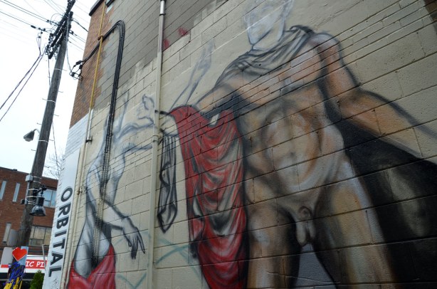 Street art piece of a semi clad woman and a male nude, reaching for each other. They are larger than life, and higher up on a wall.