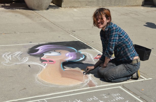 A young woman is sitting on the sidewalk. She is creating a picture of one of the characters from the TV show Futurama.
