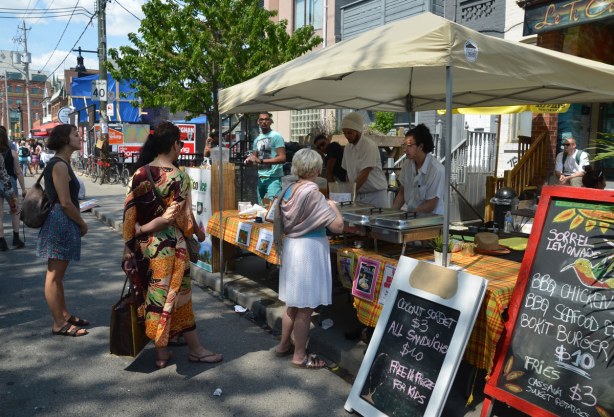 Three women are lined up waiting to be served at a street vendor who is selling food.
