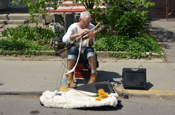 A man sitting on a stool on the sidewalk, playing a musical instrument